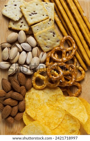 Assortment of crispy appetizers. Almonds, pistachios, Crackers, potato chips and mini pretzels. Wooden plate with Salty snacks on a white background. Party mix. top view. vertical
