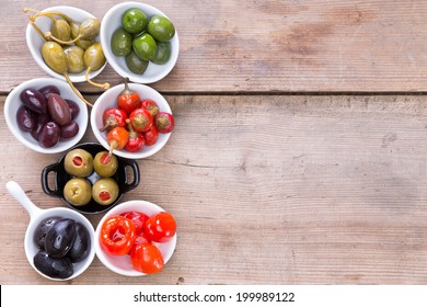 Assortment Of Cured Black, Green And Stuffed Savory Olives And Colorful Red Pimento Peppers In Small Bowls Grouped Together On An Old Wooden Bar Counter With Copy Space, Overhead View