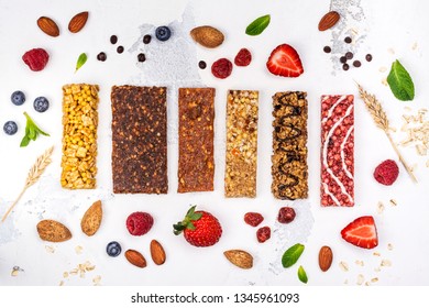 Assortment Of Different Granola Cereal Bars On White Stone Background. Healthy Pre Or Post Workout Snacks With Fruits, Nuts And Berries. Copy Space. Top View