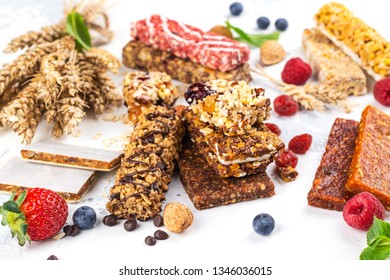 Assortment Of Different Granola Cereal Bars On White Stone Background. Healthy Pre Or Post Workout Snacks With Fruits, Nuts And Berries. Copy Space. Top View