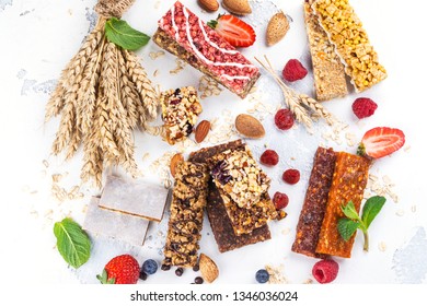 Assortment Of Different Granola Cereal Bars On White Stone Background. Healthy Pre Or Post Workout Snacks With Fruits, Nuts And Berries. Copy Space. Top View