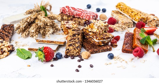 Assortment Of Different Granola Cereal Bars On White Stone Background. Healthy Pre Or Post Workout Snacks With Fruits, Nuts And Berries. Copy Space. Top View