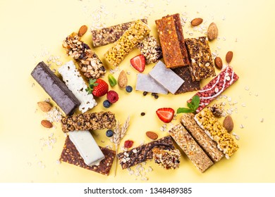 Assortment Of Different Granola Cereal Bars On Yellow Background. Healthy Pre Or Post Workout Snacks With Fruits, Nuts And Berries. Copy Space. Top View