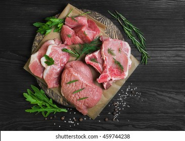 Assortment different types assorted of cuts and portions of raw fresh red meat pork displayed with fresh herbs, spice, dark brown wooden background, top view