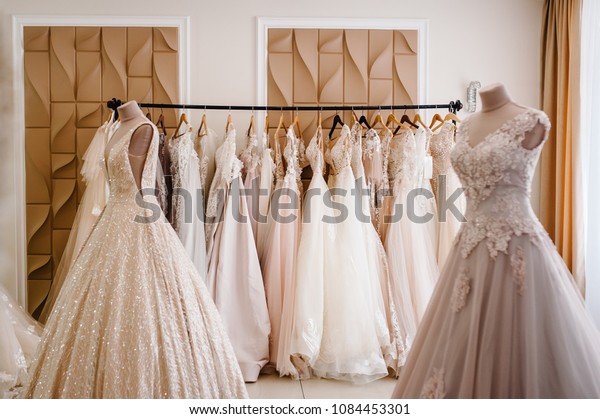 Assortment of\
dresses hanging on a hanger on the background studio. Fashion\
wedding trends. Interior of wedding\
shop.