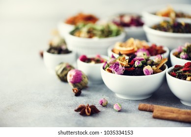 Assortment Of Dry Tea In White Bowls. Tea Types Backgound: Green, Black, Floral, Herbal, Mint, Melissa, Ginger, Apple, Rose, Lime Tree, Fruits, Orange, Hibiscus, Raspberry, Cornflower, Cranberry.