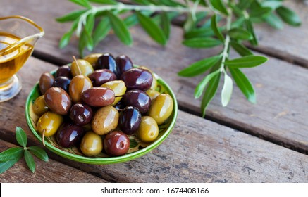 Assortment of fresh olives on a plate with olive tree brunches. Wooden background. Close up. Copy space.
