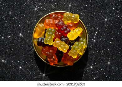 Assortment of gummy bears in a round ting box on a glittering black background