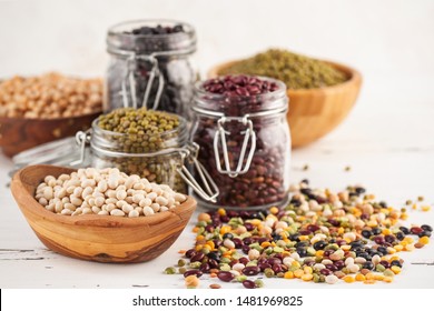 Assortment Of Haricot Beans In Glass Jars And Wooden Bowls On White Wooden Background. Variety Of Raw Legumes. Balanced Diet, Cooking, Vegetarian And Clean Eating Concept. Healthy Food.