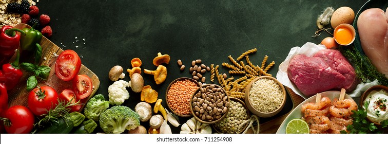 An assortment of healthy, organic, paleo harvest produce, legumes, meats and vegetables on a dark grey background with copy space in a panoramic orientation.