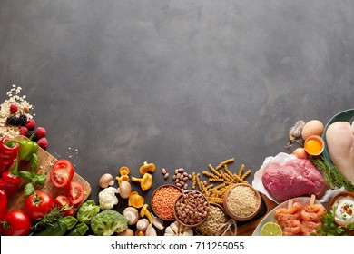 An assortment of healthy, organic, paleo harvest produce, legumes, meats and vegetables on a dark rustic grey background with copy space.