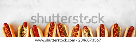 Assortment of hot dogs with a variety of toppings. Top view bottom border on a white marble background.