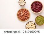 Assortment of legumes in bowls on a light background, top view. Horizontal, free space for text. Mung beans, chickpeas, peanuts, beans, lentils
