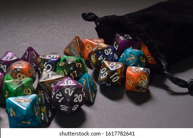 assortment of multi colored polyhedral RPG dice spilling out of black velvet pouch