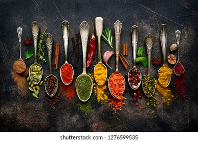 Assortment of natural spices on a vintage spoons over dark slate, stone, concrete or metal background.Top view with copy space.