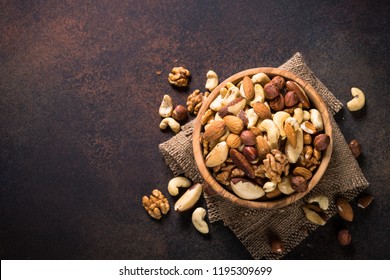 Assortment of nuts in wooden bowl on dark stone table. Cashew, hazelnuts, walnuts, almonds, brazilian nuts and pine nuts. Top view with copy space. - Shutterstock ID 1195309699