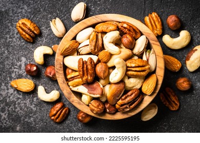 Assortment of nuts in wooden bowl on dark stone table. Cashew, hazelnuts, almonds, brazilian nuts and pecans. - Shutterstock ID 2225595195