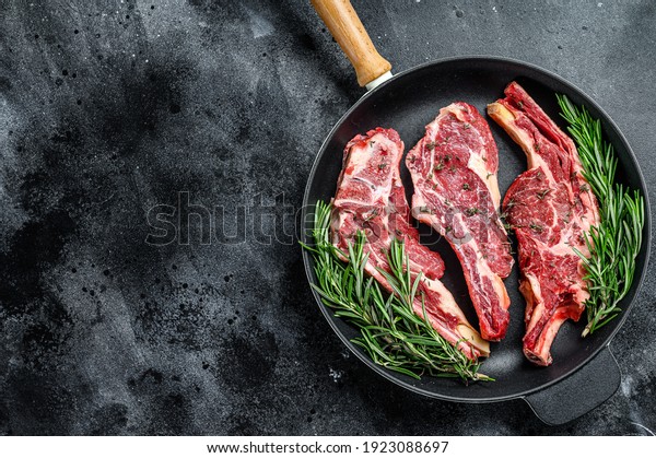 Assortment of raw cuts beef meat steaks in a\
pan. Black background. Top view. Copy\
space