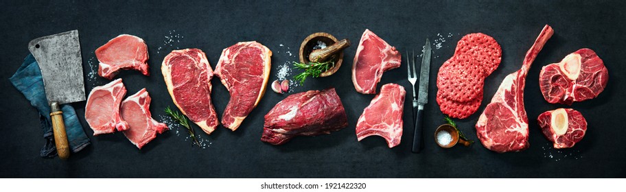 Assortment of raw cuts of meat, dry aged beef steaks and hamburger patties for grilling with seasoning and utensils on dark rustic board