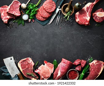 Assortment of raw cuts of meat, dry aged beef steaks and hamburger patties for grilling with seasoning and utensils on dark rustic board - Powered by Shutterstock