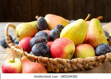 An assortment of raw fruit in a basket on a gray wooden table. Lots of plums, peaches, apples and pears. Healthy food concept	