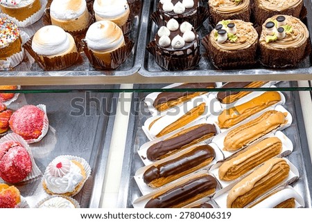 Assortment of small cakes and eclairs displayed in a bakery case.