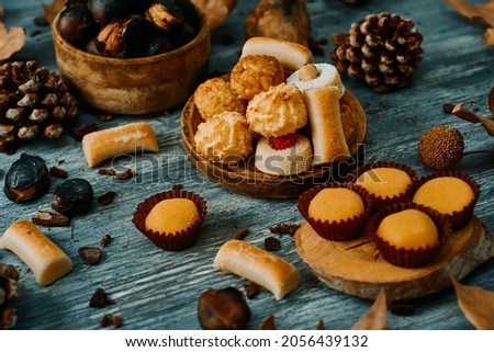 an assortment of some different confections eaten in Spain on All Saints Day, such as Panellets, Huesos de Santo or Yemas de Santa Teresa, and some roasted chestnuts on a gray rustic table