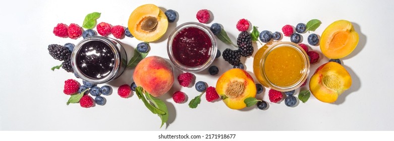 Assortment of summer seasonal berry and fruits jams in small jars, homemade preserving concept, marmalades or confitures with fresh berries on white background copy space