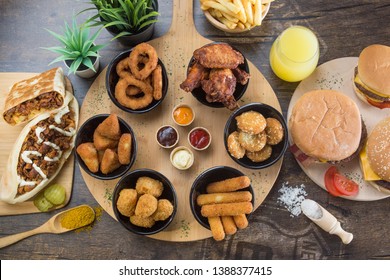 Assortment of Tex Mex dishes with sauces, accompanied by french fries and orange juice. Served on a round wooden board with burgers, tacos and kebabs.