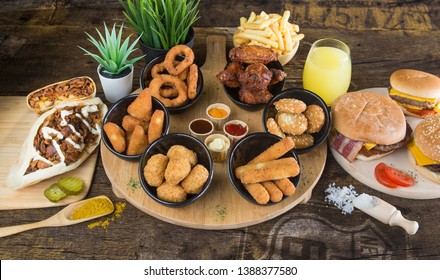 Assortment Of Tex Mex Dishes With Sauces, Accompanied By French Fries And Orange Juice. Served On A Round Wooden Board With Burgers, Tacos And Kebabs.