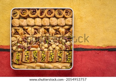 assortment of traditional Turkish baklava pastry in a tin box, a dessert is well also known as Persian or Lebanese baklava, textured paper background with a copy space