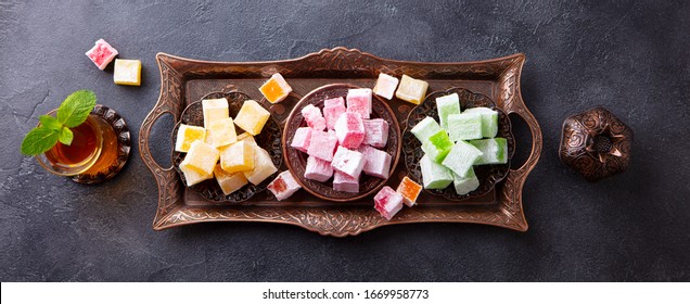 Assortment of Turkish delights on a copper tray with glass of tea. Grey background. Top view.