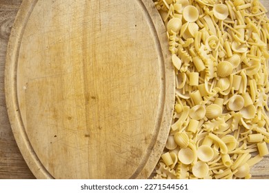 assortment of uncooked pasta next to an empty wooden cutting board - Powered by Shutterstock