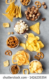 Assortment of Unhealthy Snacks: chips, popcorn, nachos, pretzels, onion rings in bowls, top view, flat lay. Unhealthy eating concept.