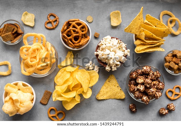Assortment of Unhealthy Snacks: chips, popcorn,\
nachos, pretzels, onion rings in bowls, top view, copy space.\
Unhealthy eating\
concept.