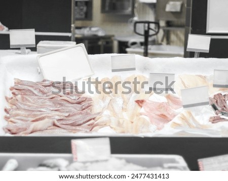 An assortment of varieties of white sea fresh fish lies on the counter in a store with empty pegs for your text, close-up side view. Offline shopping concept, fish business, fish trading.