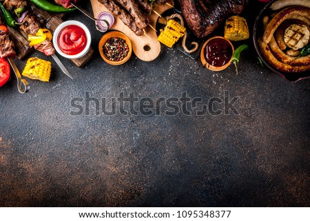 Assortment various barbecue food grill meat, bbq party fest - shish kebab, sausages, grilled meat fillet, fresh vegetables, sauces, spices, dark rusty concrete table, above copy space