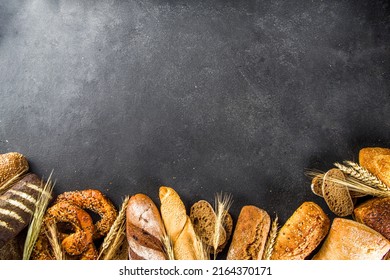 Assortment of various delicious freshly baked bread, on black concrete background top view copy space