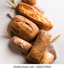 Assortment of various delicious freshly baked bread on white background. Variety of artisan bread composition and ears of wheat.