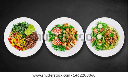 Assortment of various healthy keto paleo meals on white plate. Black stone background. Top view. Isolated. Space for text.