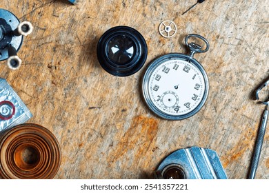 assortment of watchmaking tools surrounds a pocket watch on a worn wooden surface, displaying components like a gasket coil, magnifier, and gear, highlighting precision work - Powered by Shutterstock