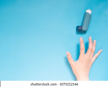 Asthma And COPD Disease Concept. Young Female Hand Trying To Reach Blue Asthma Inhaler For Relief Asthma Attack Symptoms On Light Blue Background With Copy Space For Text. Top View. Minimal Style.