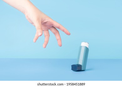 Asthma And COPD Disease Concept. Young Female Hand Trying To Reach Blue Asthma Inhaler For Relief Asthma Attack Symptoms On Light Blue Background. Minimal Style.