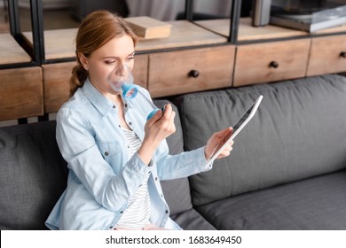 Asthmatic Woman Using Inhaler With Spacer And Holding Digital Tablet