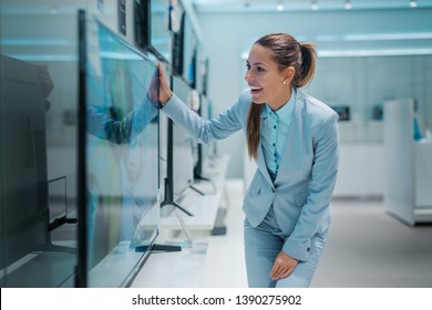 Astonished Caucasian Brunette In Formal Wear Found A Tv She Want To Buy. Tech Store Interior.