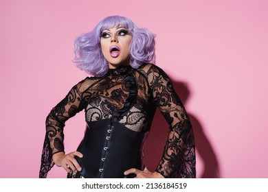 astonished drag queen in purple wig standing with hands on hips on pink - Powered by Shutterstock