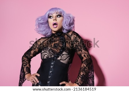 astonished drag queen in purple wig standing with hands on hips on pink