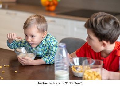 Astonished kid staring at his sibling gobbling down his breakfast
