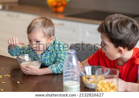 Astonished kid staring at his sibling gobbling down his breakfast