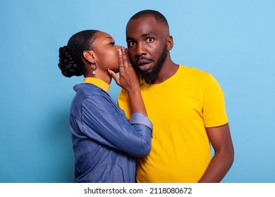 Astonished man finding out secret rumour from girlfriend in studio. Young woman whispering gossip in ear of boyfriend, having confidential conversation. Curious person listening to mistery.